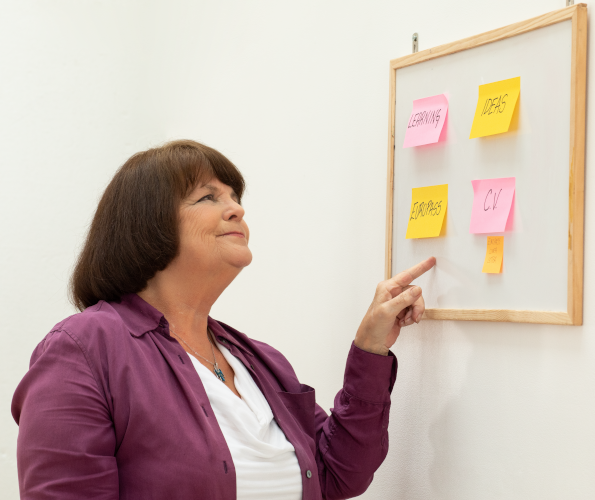 Woman pointing at a white board with sticky notes about learning and skills